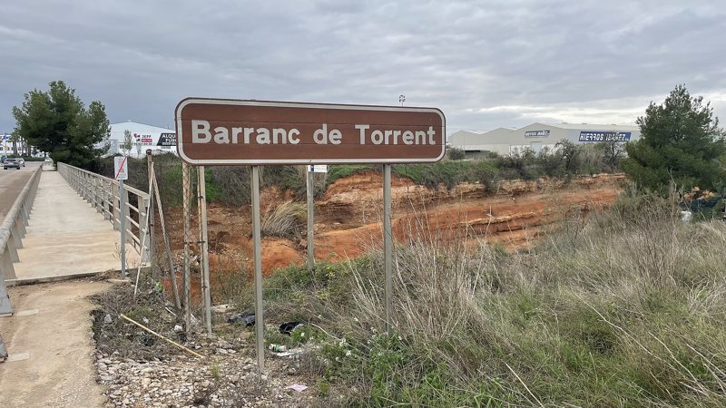 Табличка Barranc de Torrent у моста, под ней сухое русло с красной глиной